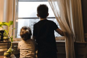 A little boy and little girl looking out a rainy window.