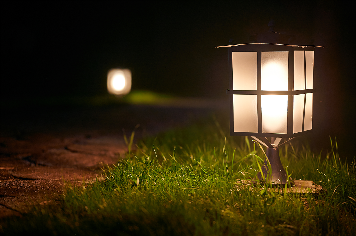 An outdoor home lighting lantern illuminating a dirt pathway.