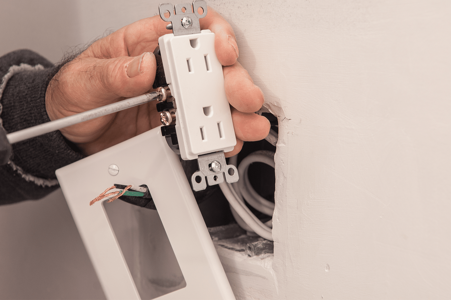 A person working on an outlet while trying to avoid electrical mistakes.