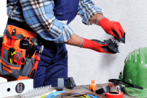 An electrician in blue overalls and red gloves working on fixing electrical mistakes.