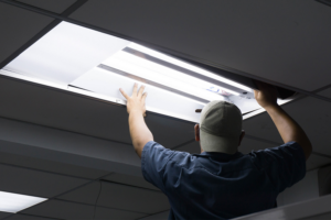 Electrician man performing electrical maintenance by fixing a commercial light