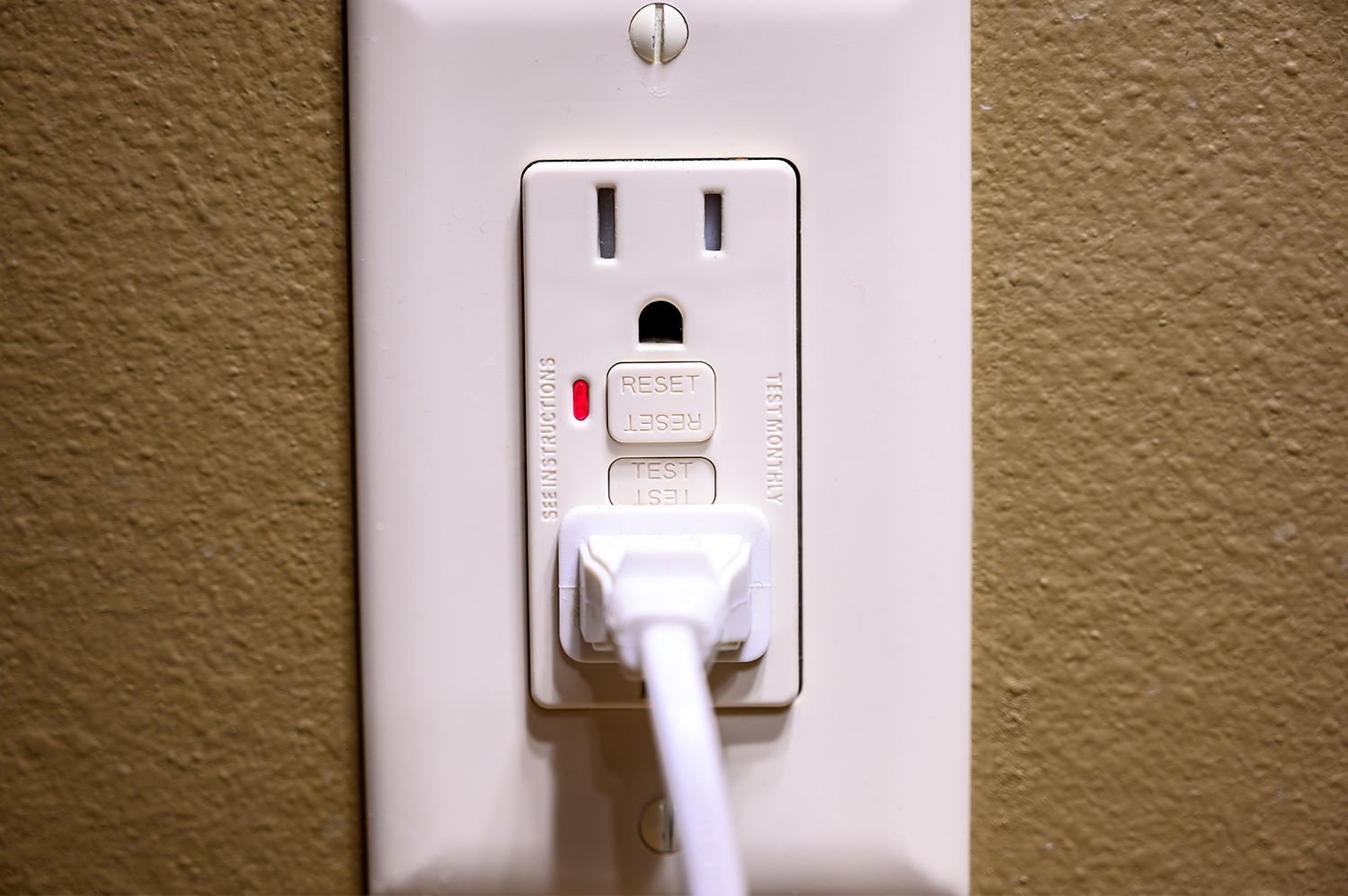 A closeup of a cord plugged into a GFCI outlet on a brown wall.