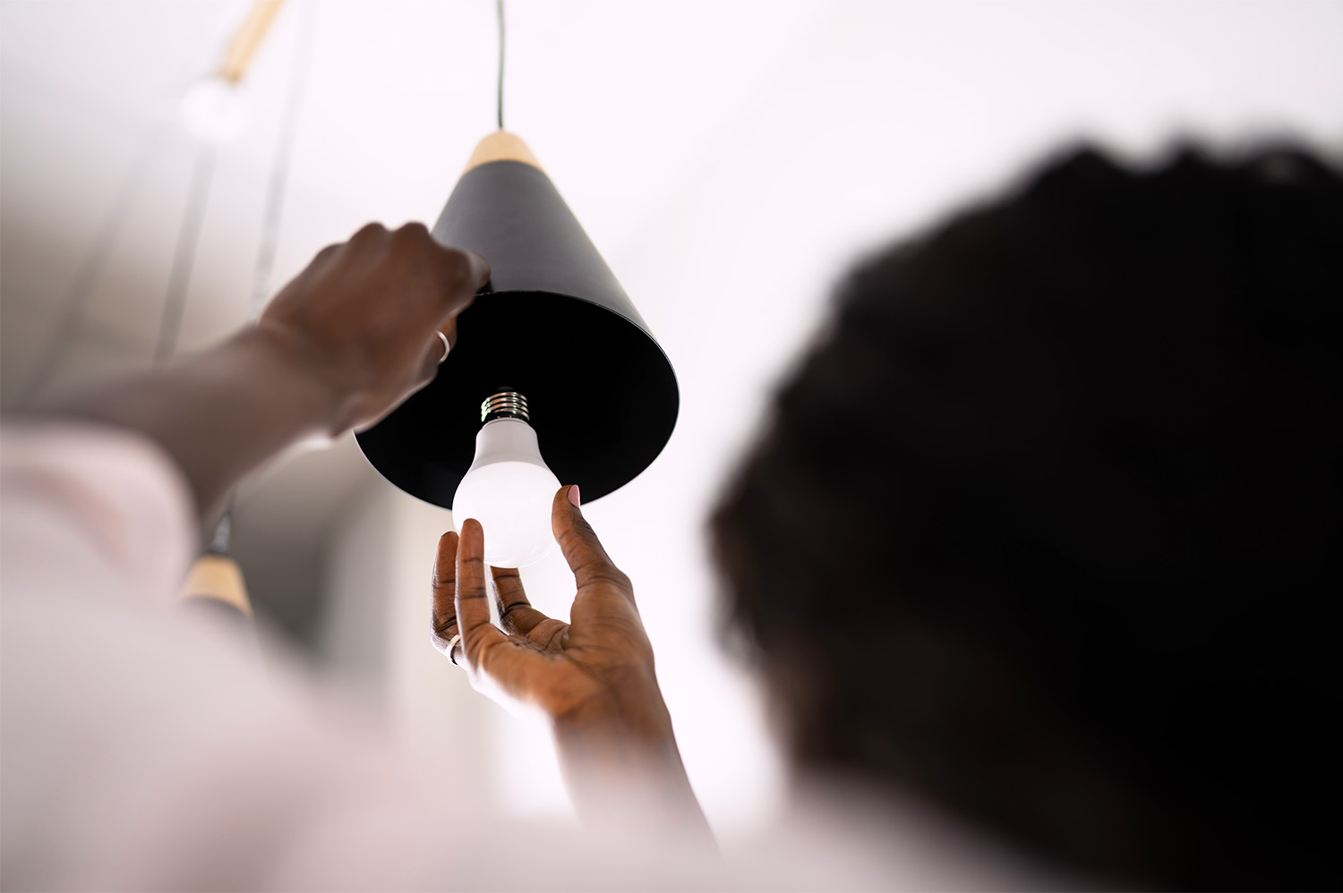 A woman changing out a lightbulb in a hanging light fixture - a task for spring cleaning.