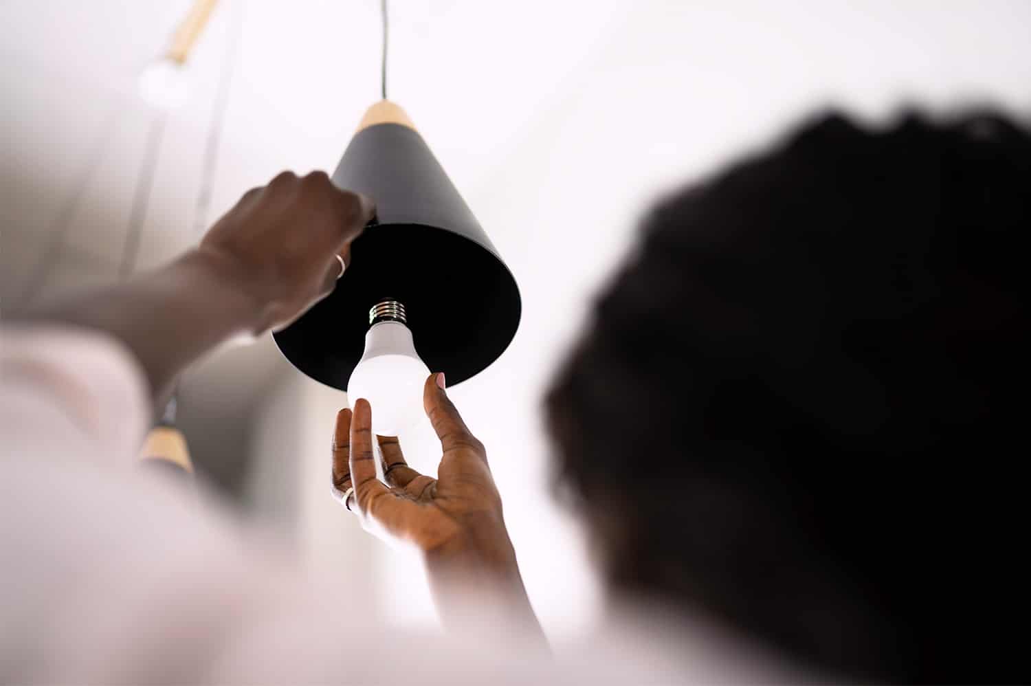 A woman changing out a lightbulb in a hanging light fixture - a task for spring cleaning.