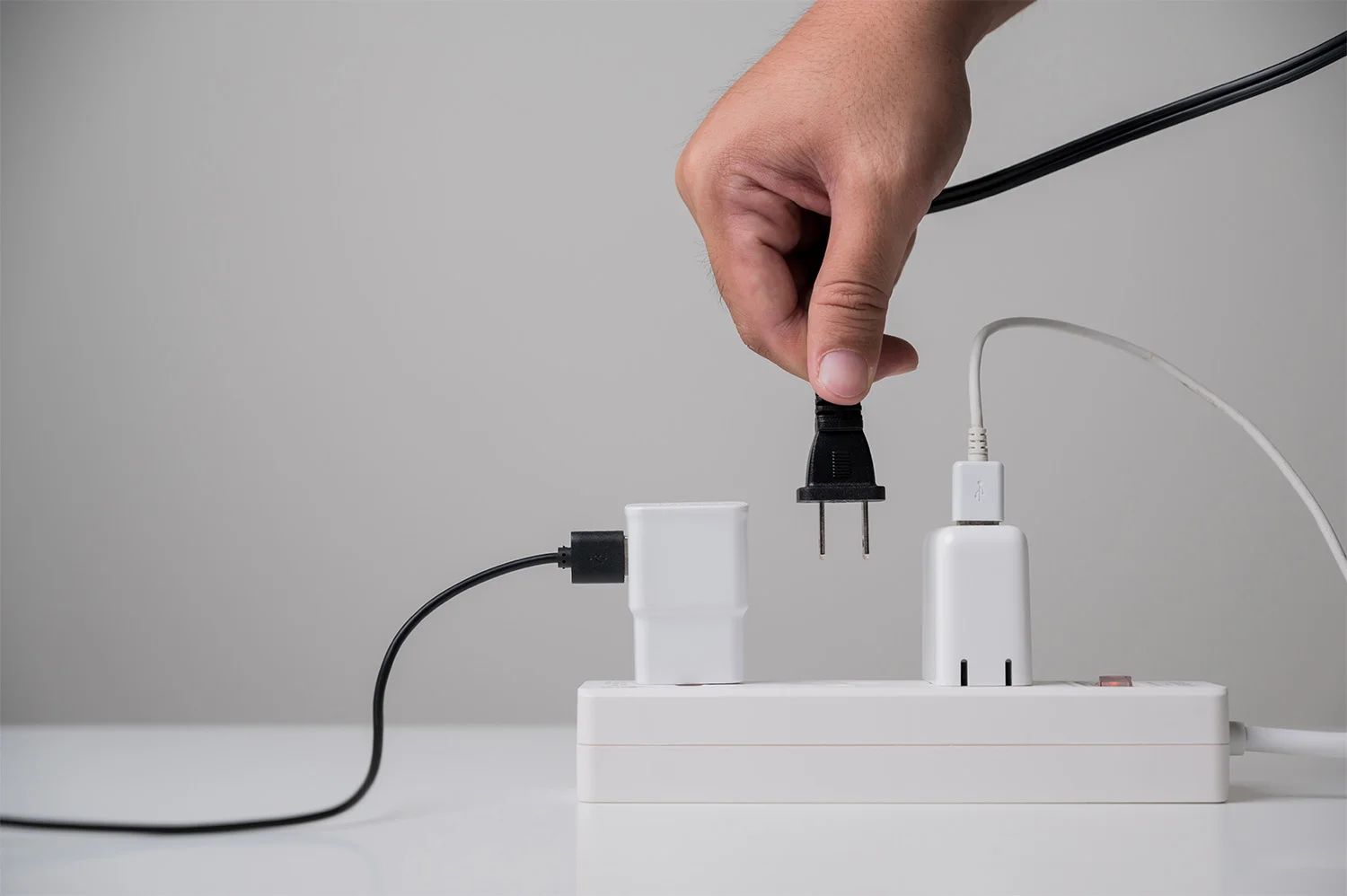 A person plugging a cord into an overloaded power strip which will lead to electrical overloads.