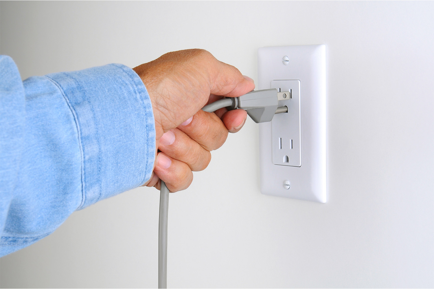 A person plugging a three pronged grey plug into an outlet.